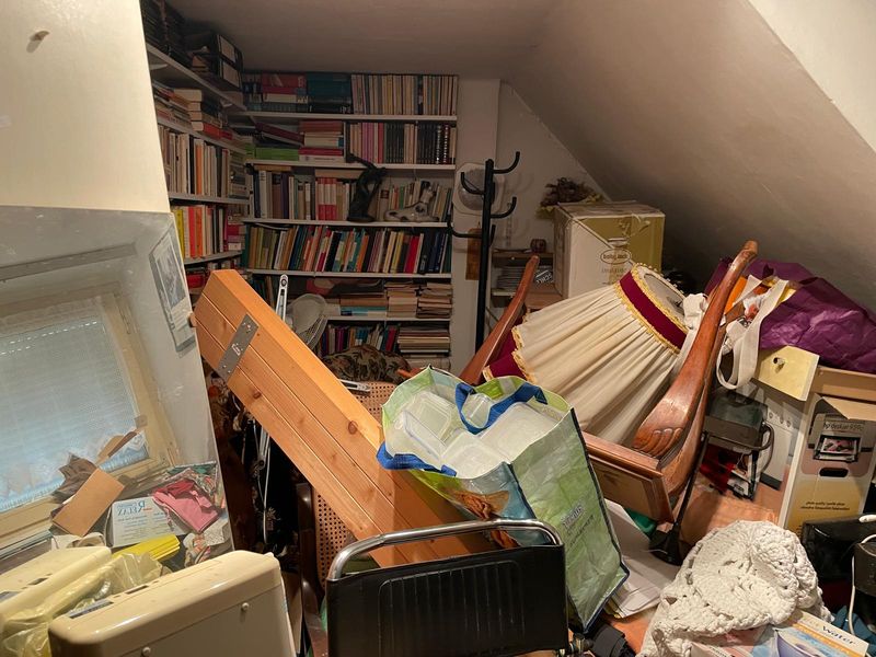 Dachzimmer voller Bücher, Kartons und Möbel vor der Entrümpelung